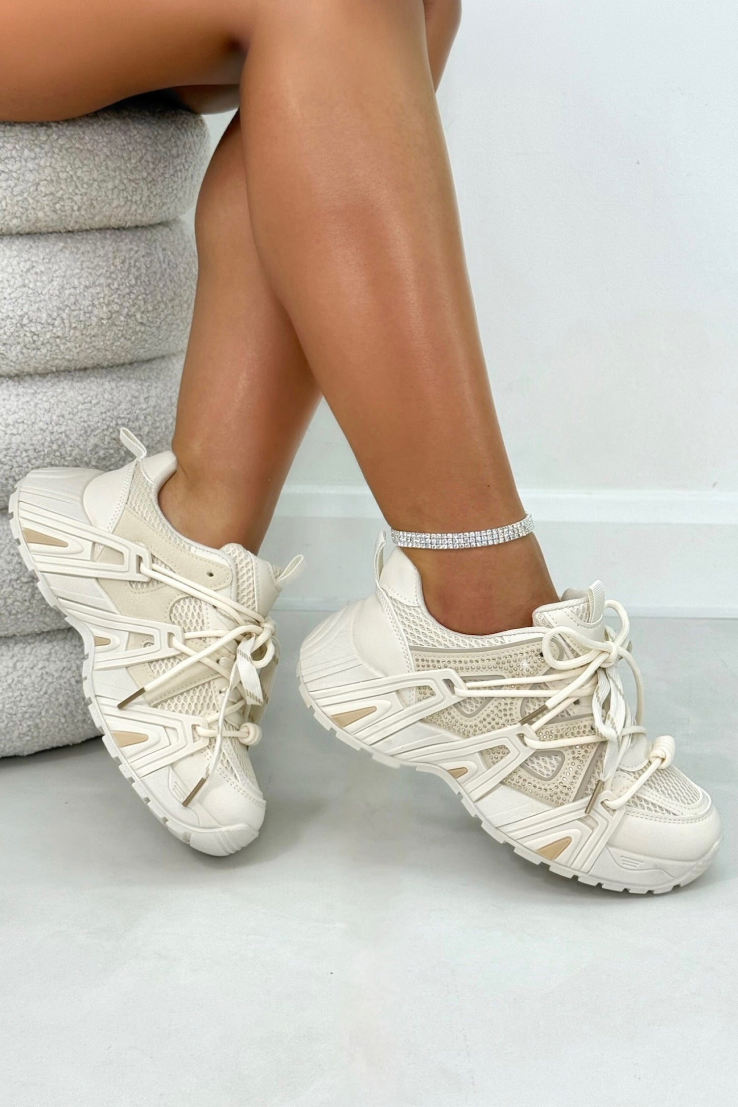Beige sneakers worn by a person sitting on a gray cushioned chair.