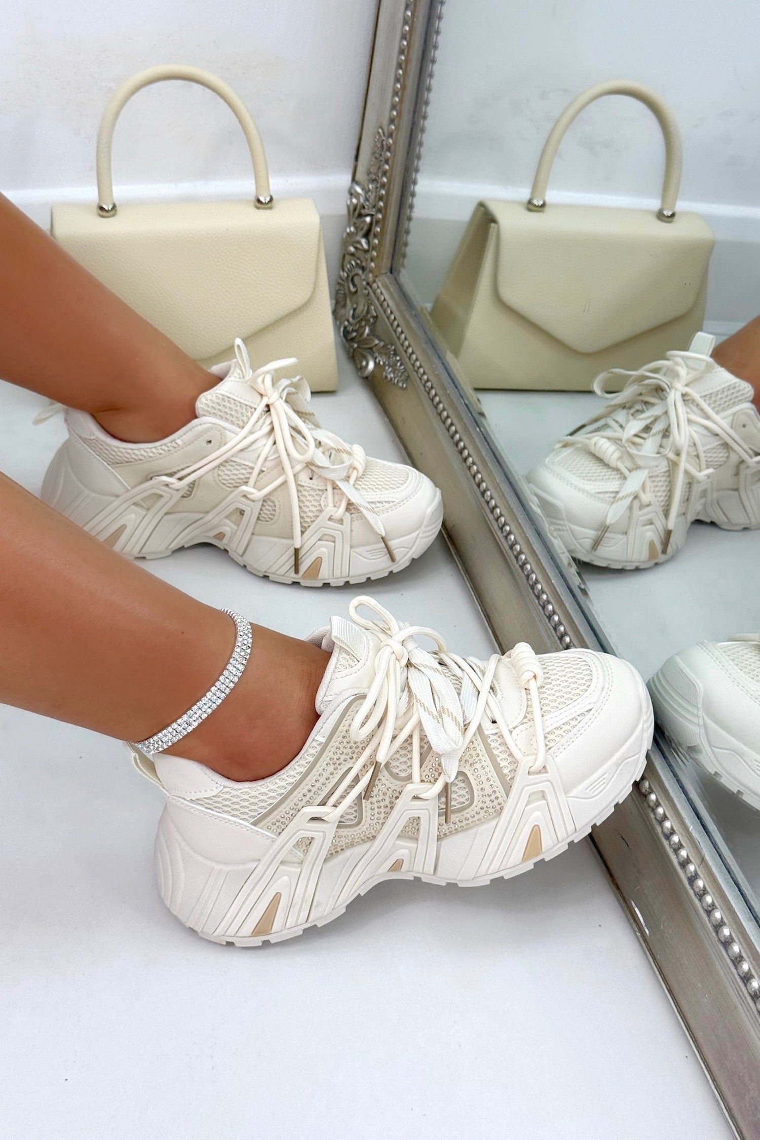 Beige sneakers worn with a beige handbag reflected in a mirror.