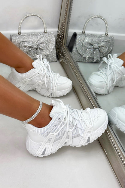 White sneakers worn with a silver glittery handbag on a light background