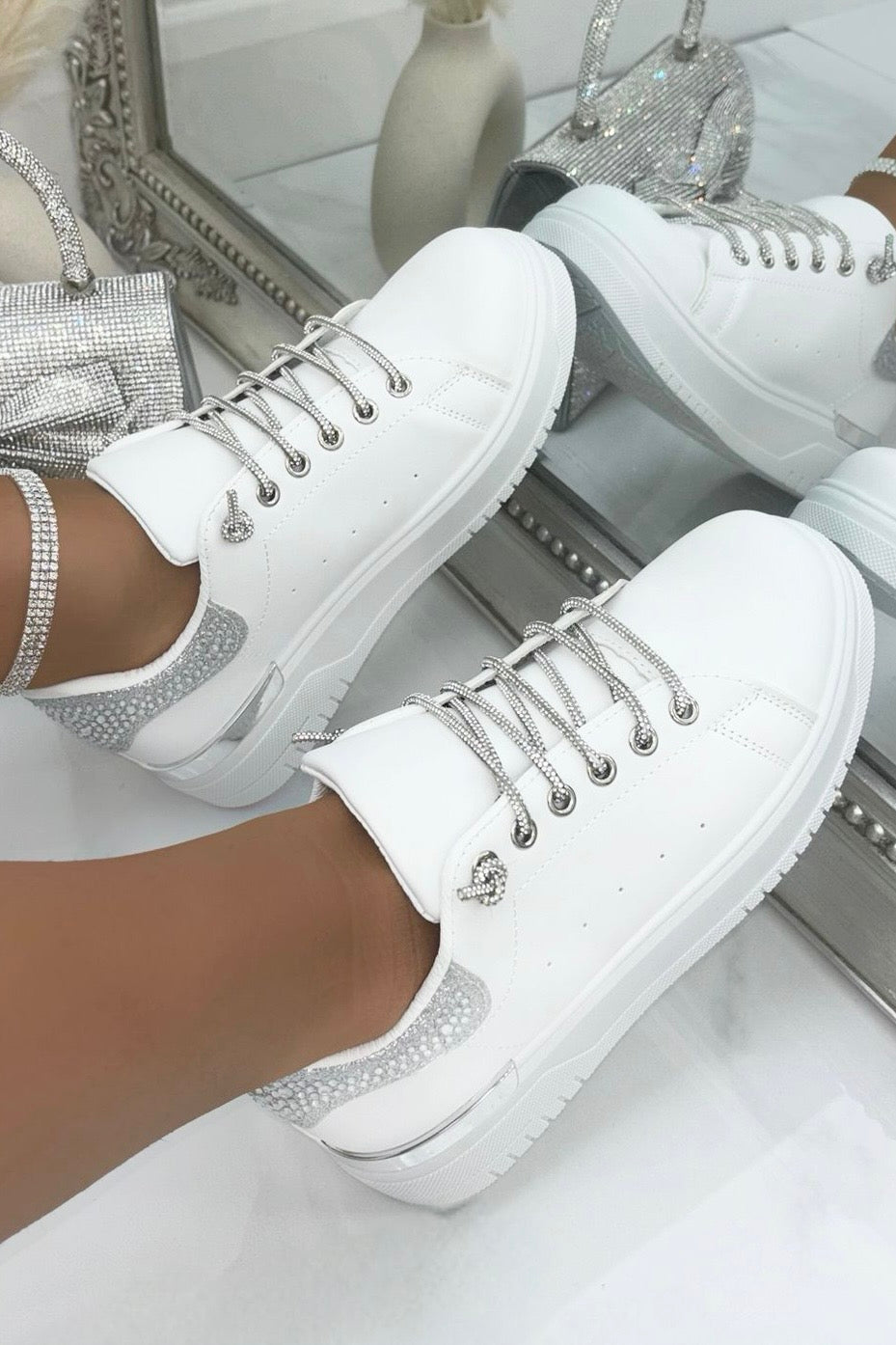 White sneakers with decorative laces and soles worn by a person, with a blurred background.