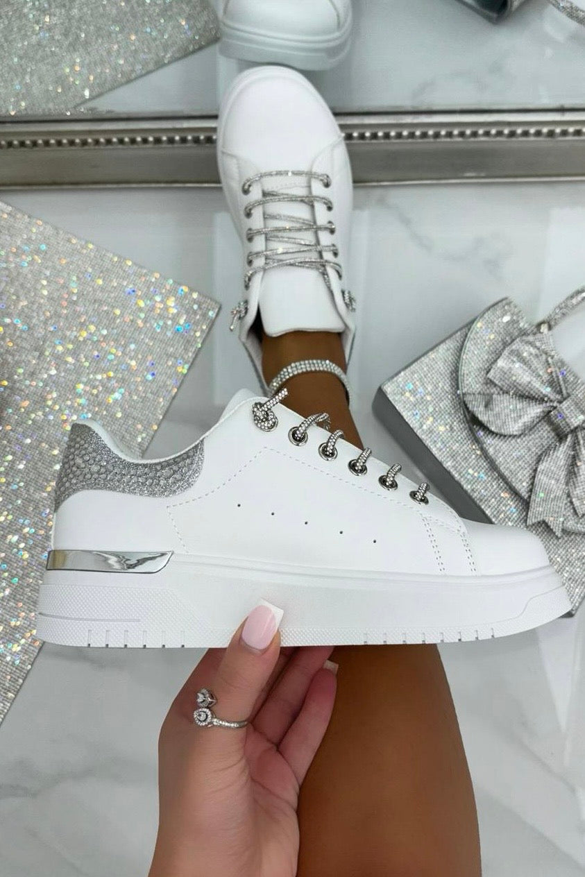 White sneakers with silver accents held by a hand against a glittery background