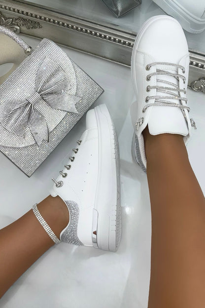 White sneakers with rhinestone details on a white surface, with a decorative box in the background.