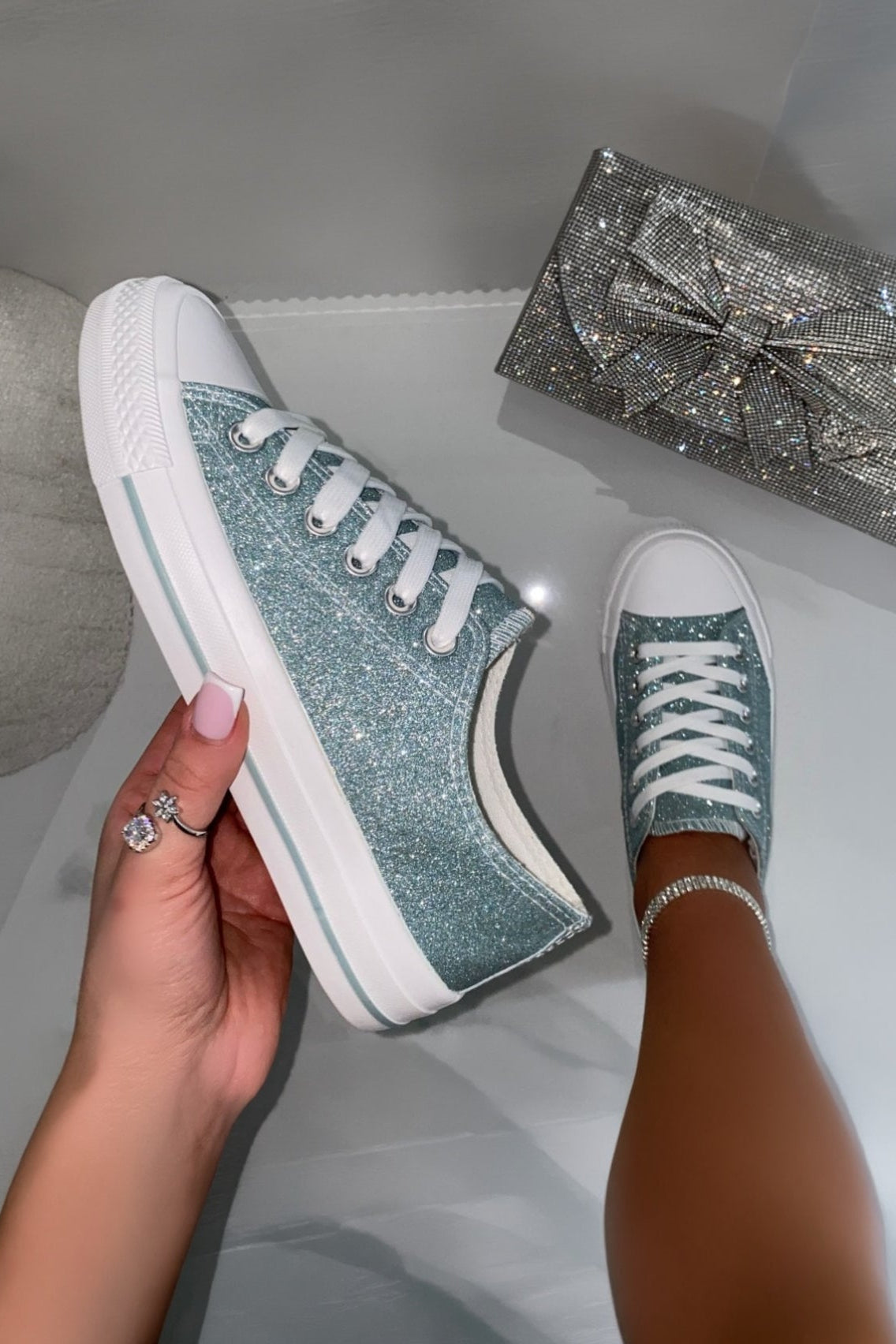 Turquoise glitter sneakers with white soles held by a hand, with a sparkling box in the background.