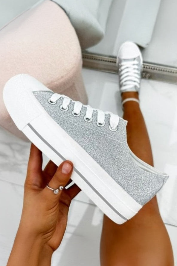 Person wearing silver sneakers with glittery details, holding one shoe.