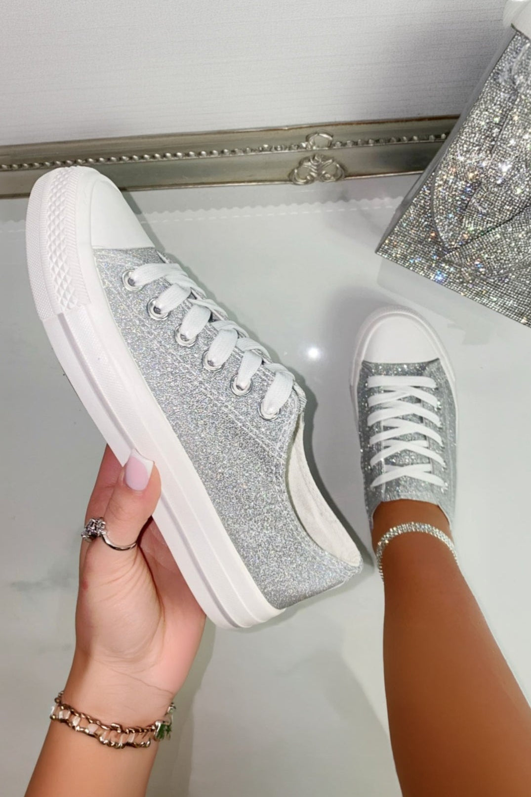 Silver glitter sneakers being held up against a white background