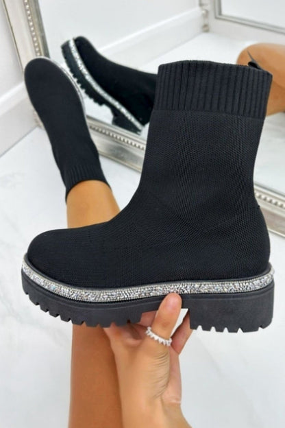 Black ankle boots with rhinestone trim held by a person against a white background