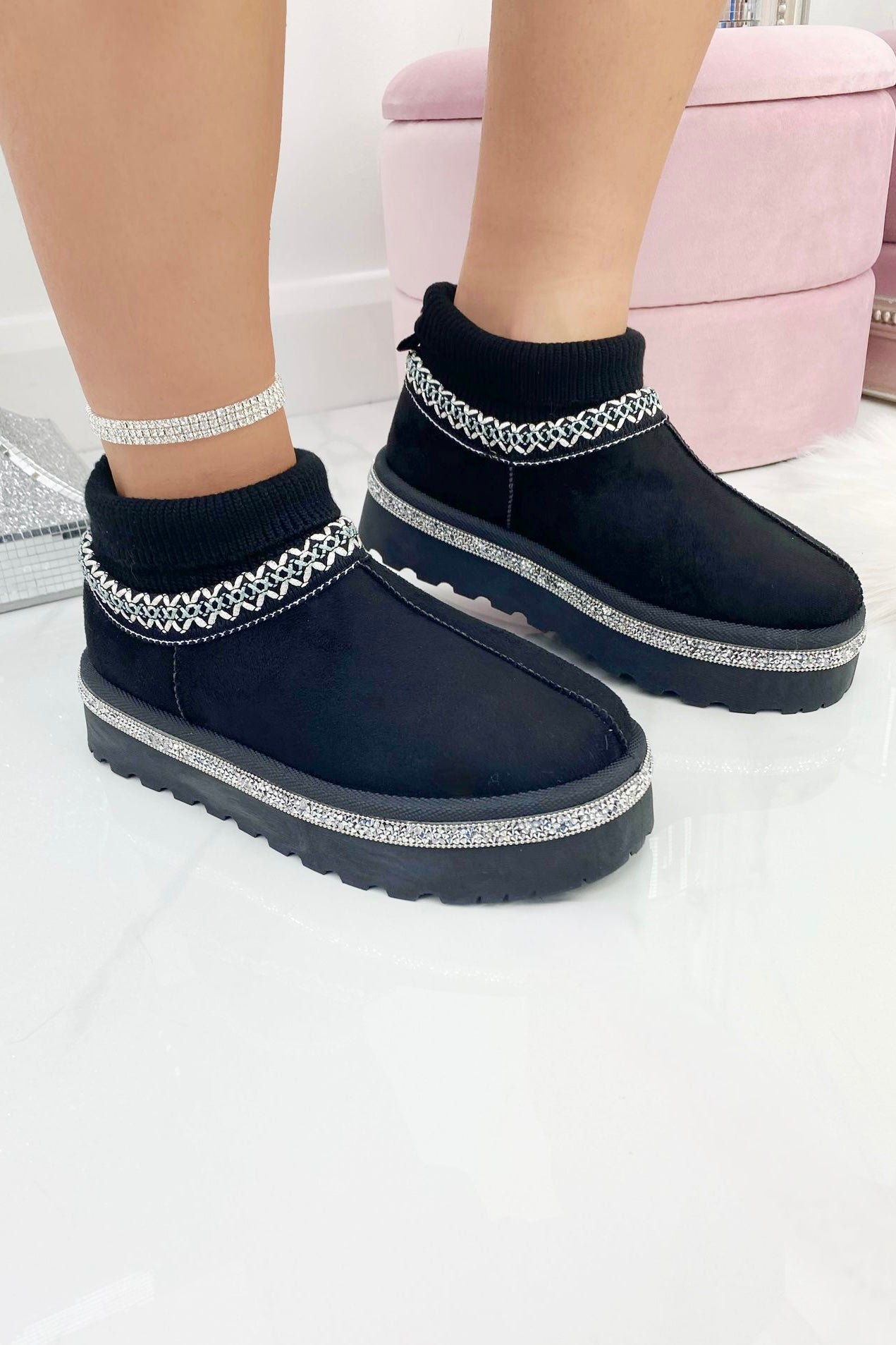 Black snow boots with silver embellishments worn by a person on a white background