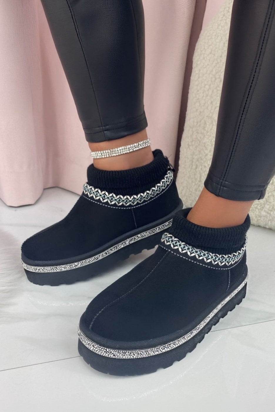 Black boots with white trim worn by a person on a light wooden floor.