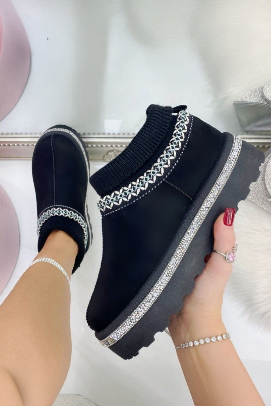 Black slip-on shoes with decorative straps held by a hand against a soft focus background