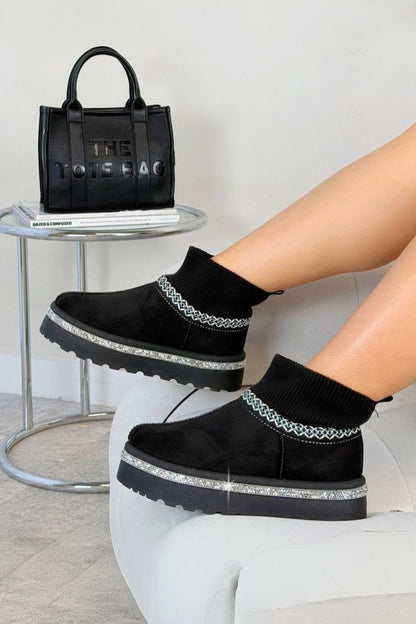 Black platform shoes with silver accents worn by a person, with a black handbag in the background.