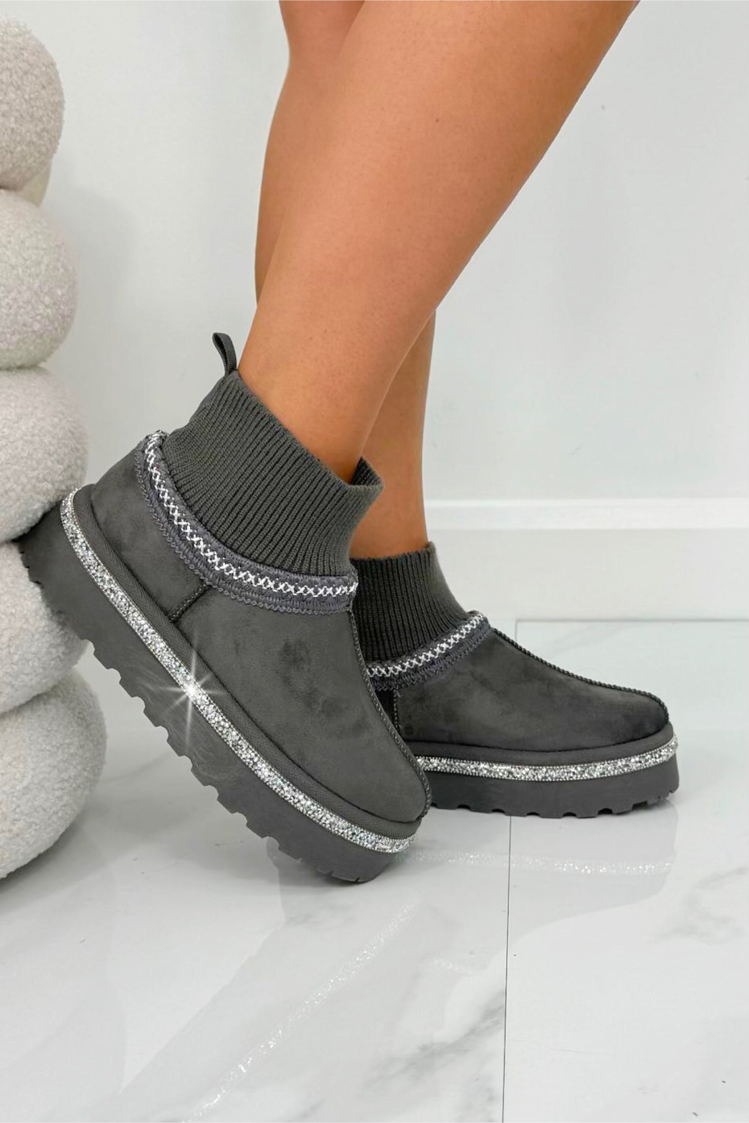 Gray suede boots with rhinestone details worn by a person on a light background