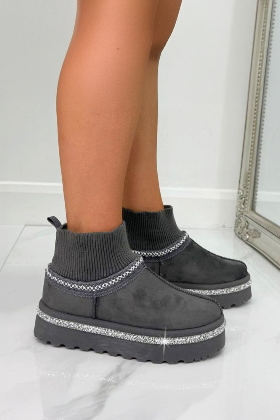 Gray platform boots with rhinestone details worn by a person on a light gray floor.