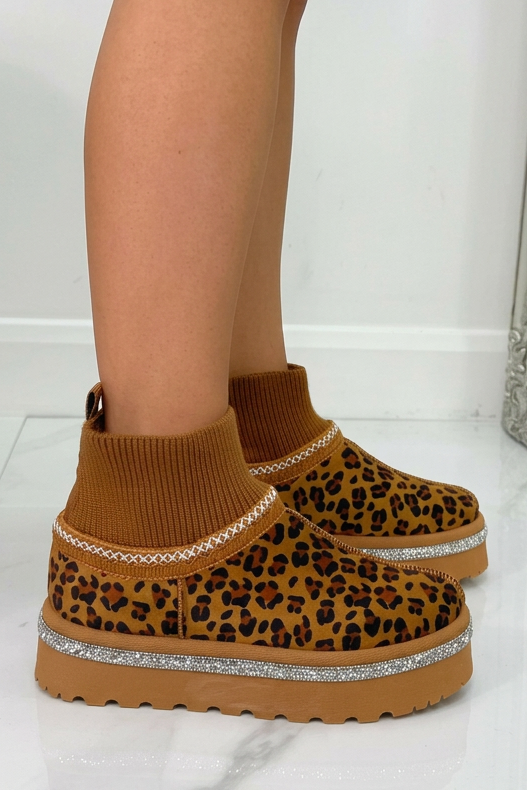 Brown platform boots with leopard print design worn by a person on a white floor.