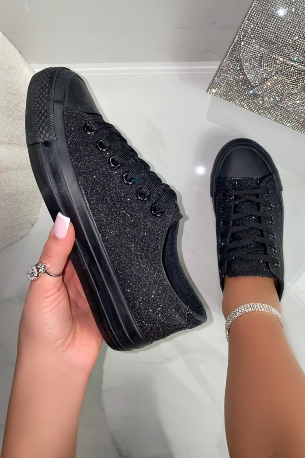 Black glittery sneakers held by a hand on a light background