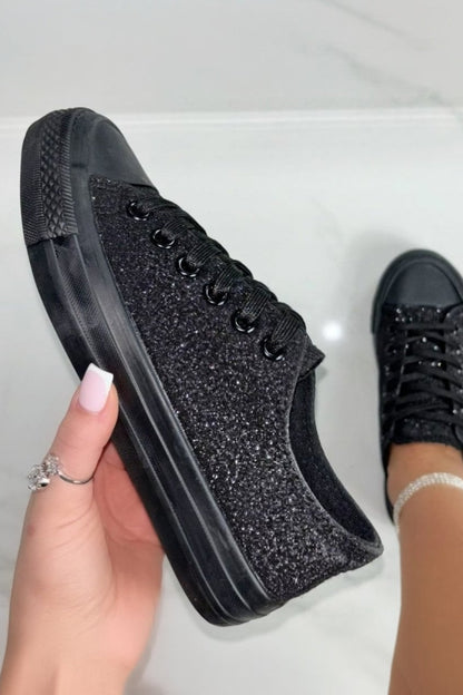 Black glittery sneakers being held by a hand on a light background