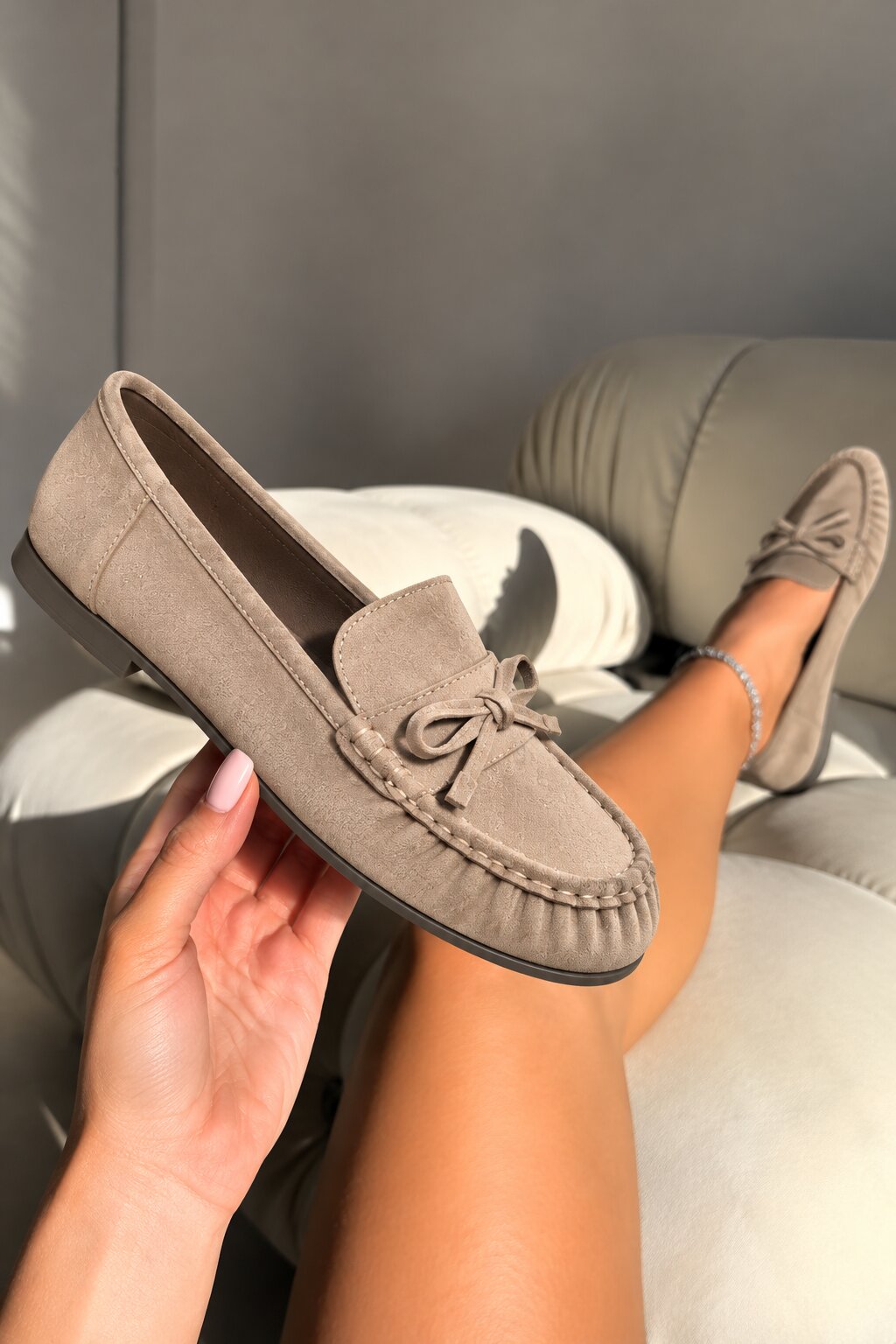A taupe suede moccasin loafer held in a hand, with the model&