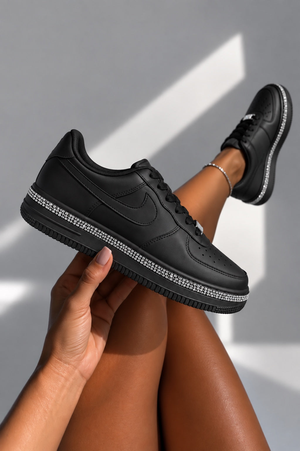 A pair of black low-top sneakers with rhinestone-trimmed soles, shown being worn and held by a person&