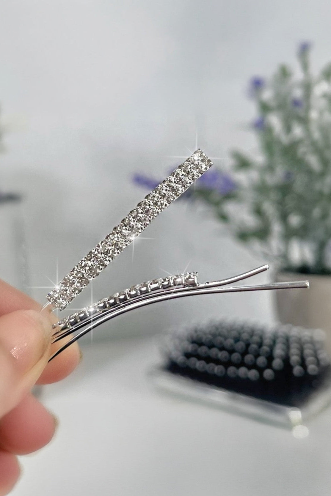 Silver hairpin with rhinestones held by a hand against a blurred background