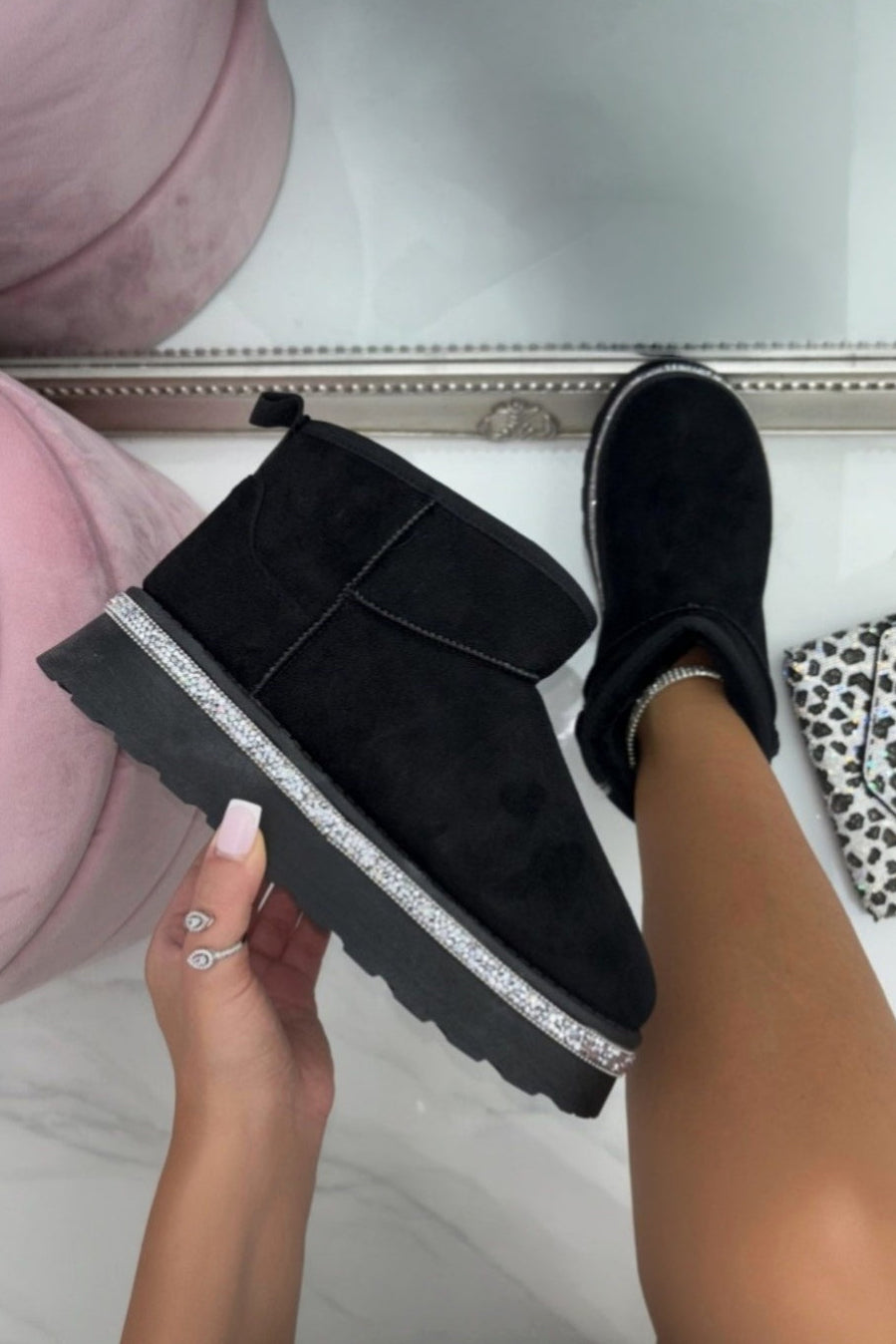 Person holding a black slip-on shoe with a glittery sole in front of pink slippers.