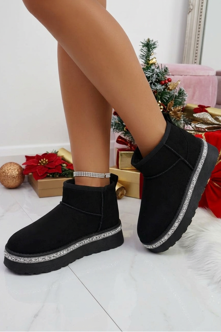 Black ankle boots with rhinestone details worn by a person, Christmas decorations in the background.
