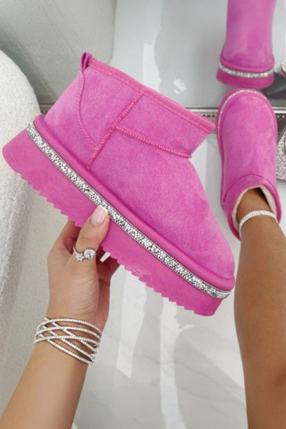 Pink faux suede boots with rhinestone trim held by a hand on a white background