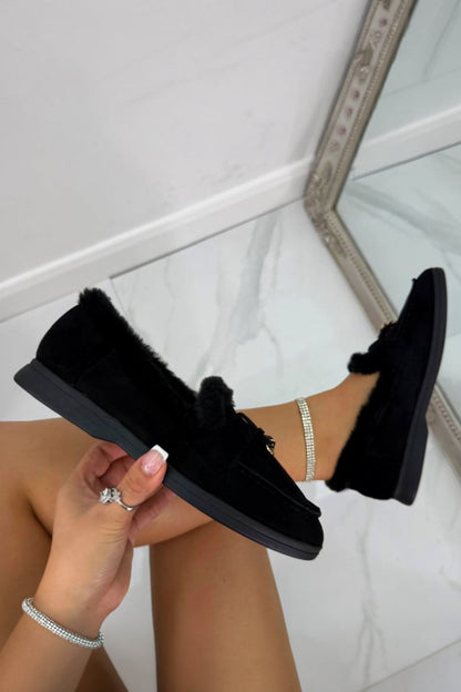 Person wearing black loafers with fur trim, holding one shoe.