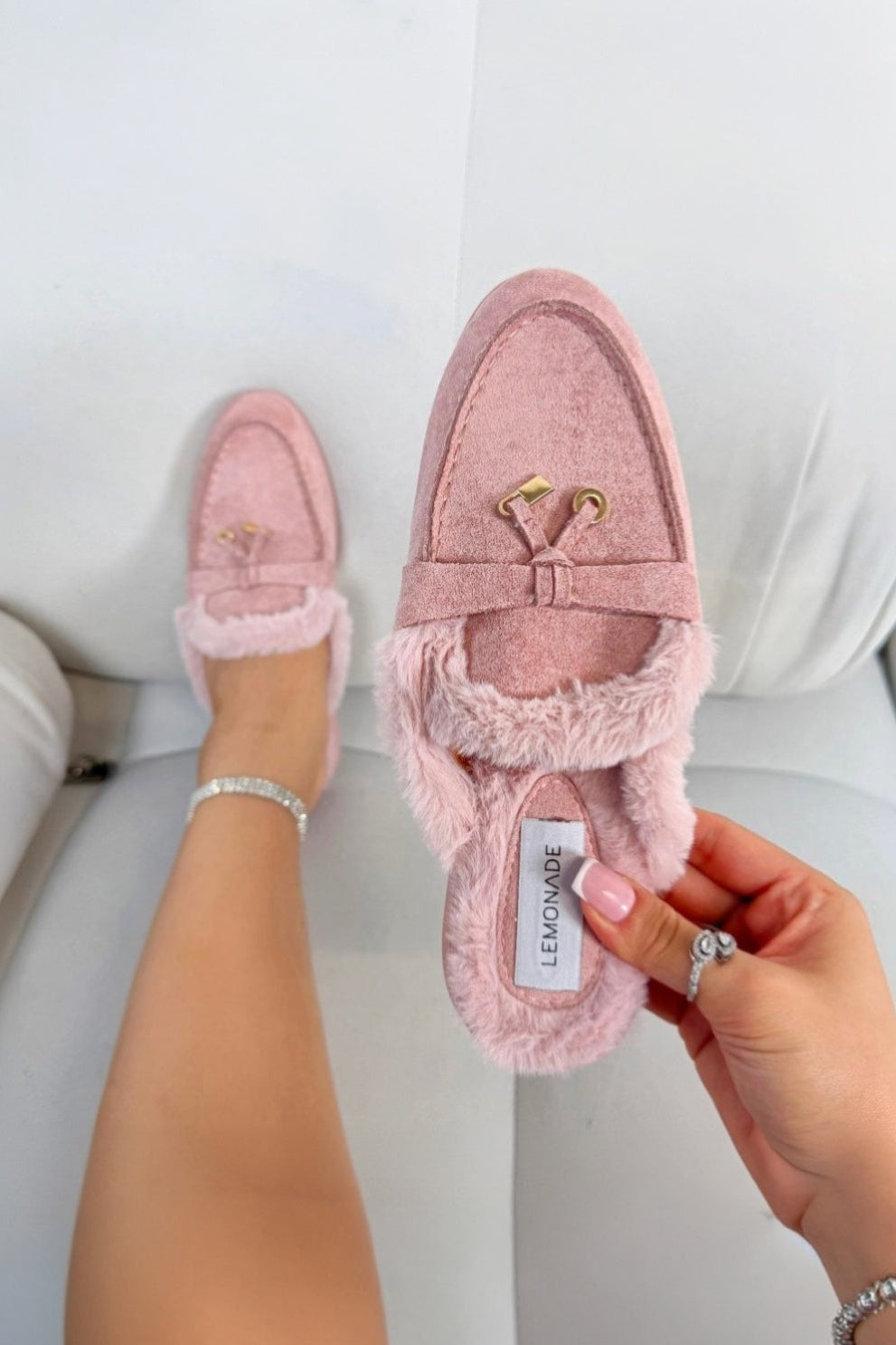 Pink slippers with fuzzy texture held by a hand on a light background