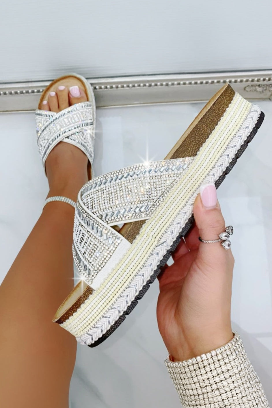 White sandal with criss-cross strap held by a hand against a light background