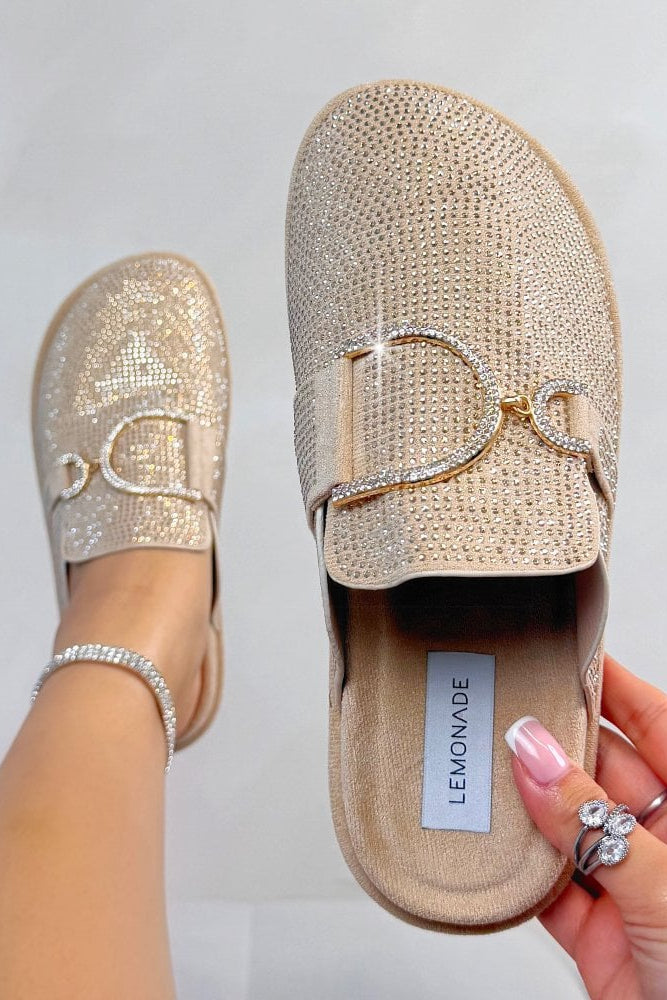 Beige glittery loafers with a decorative buckle held by a hand on a light gray background
